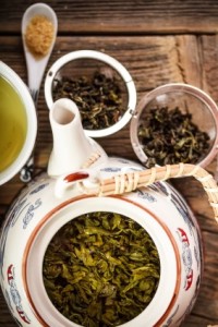 overhead image of ornate ceramic teapot with green tea and leaves