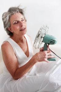 mature woman using a fan to cool off from hotflash