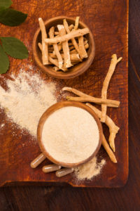 Ashwagandha powder and root on cutting board on wooden table.
