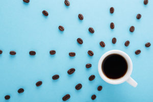 Cup of Coffee espresso with rays of coffee beans on blue background. Flat lay, creative design. Morning black coffee mood concept.