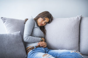 Young woman in pain lying on couch at home
