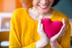 Woman  hands in yellow sweater holding pink plush heart - heart health concept