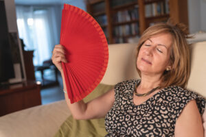 Adult woman fans herself due to the high heat produced by menopause