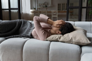 woman on couch with hands covering eyes, as in pain