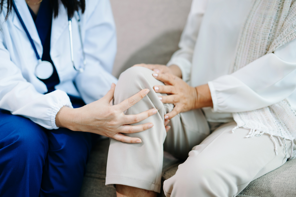 Doctor examining elderly woman with knee pain during home healthcare visit, highlighting arthritis treatment, senior support, medical consultation and compassionate care.